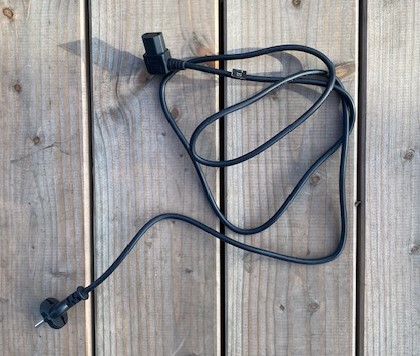 Schwarzes Kabel mit Stecker, auf einem Holztisch liegend.